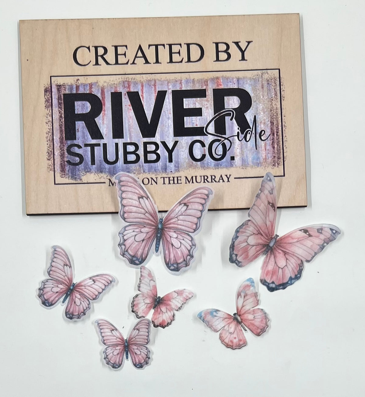 Purple edible wafer paper butterfly cake charms arranged below a Riverside Stubby Co wooden sign