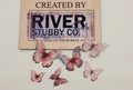 Purple and pink edible wafer paper butterfly cake charms arranged below a Riverside Stubby Co wooden sign